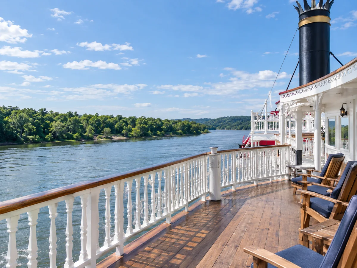 The open top deck of a paddlewheel riverboat with white railings above a green river